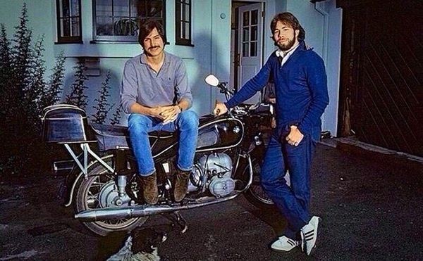 Steve Jobs sitting on a motorcycle with Steve Wozniak standing beside